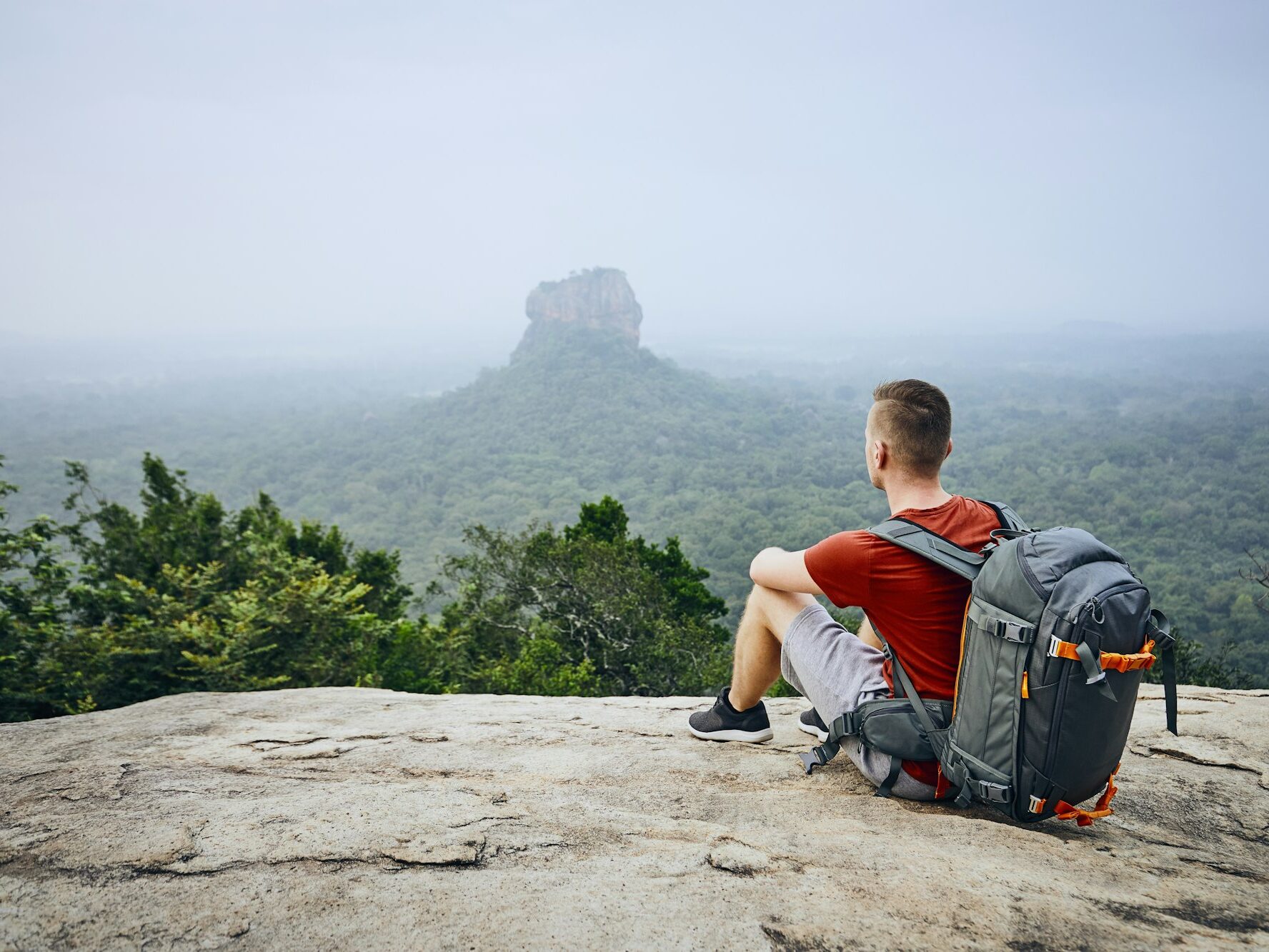 Young man with backpack against Sigiriya Rock (UNESCO World Heritage Site)